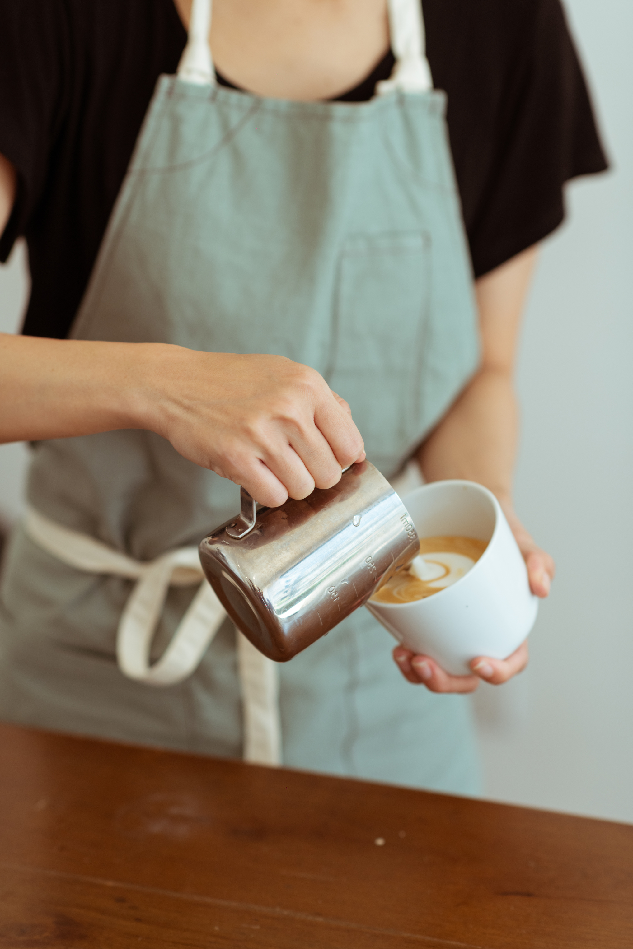 Crop barista pouring milk in cup with cappuccino